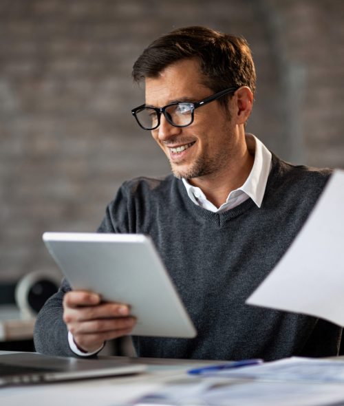Happy businessman using touchpad and laptop while working on business reports in the office.